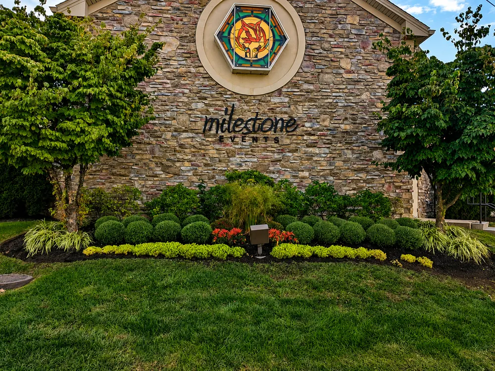 Stone entrance monument framed by manicured shrubs and seasonal color